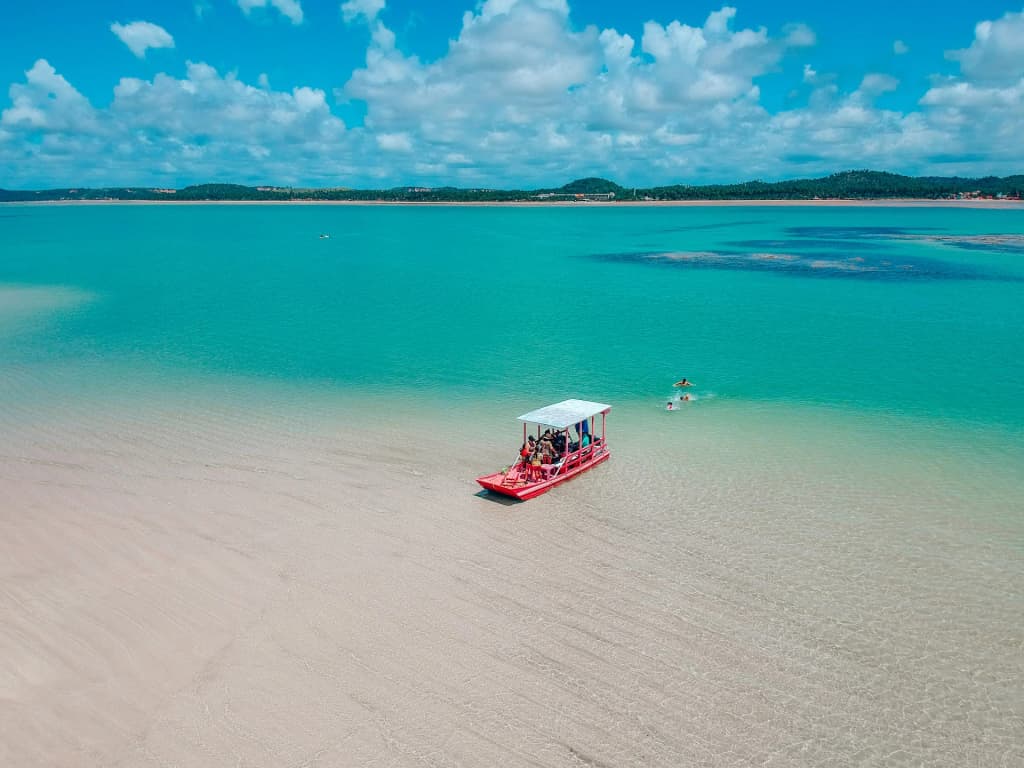 A traditional sailing raft glides over the shallow, turquoise waters of Crôas de São Bento