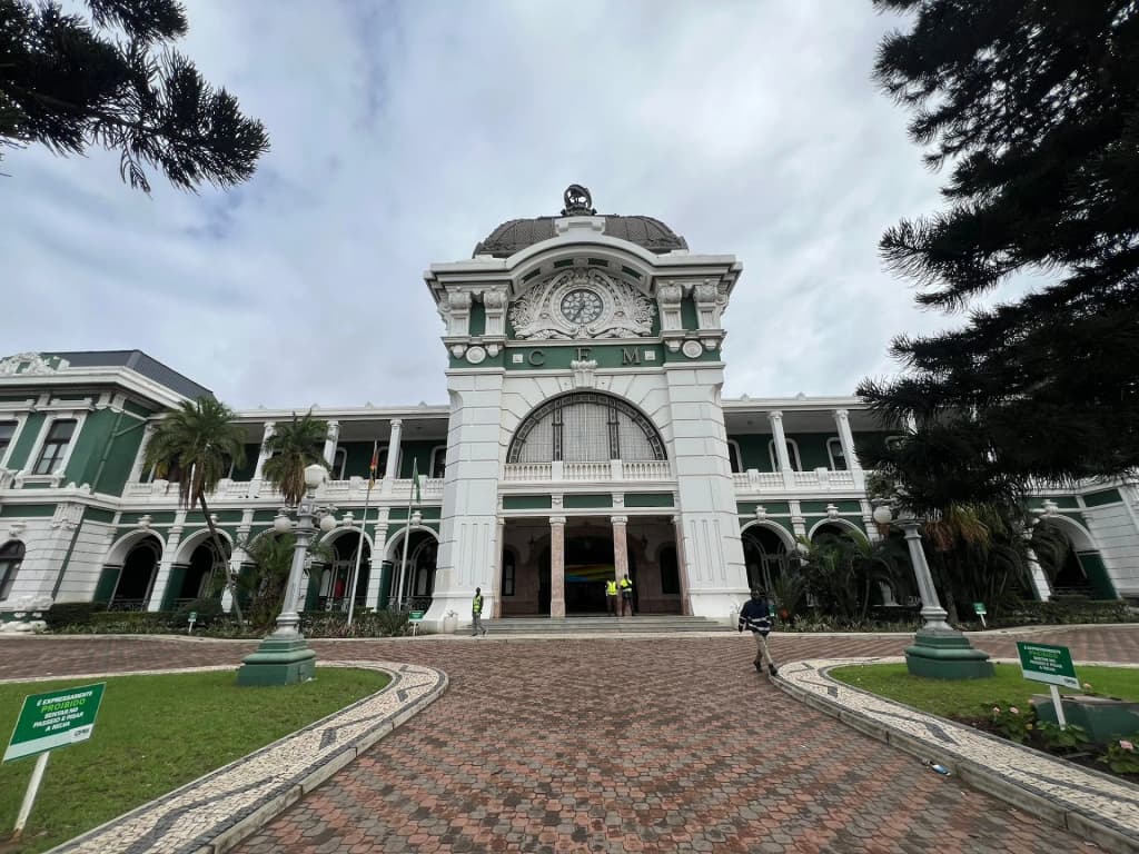 The mint-green and wrought-iron facade of the Maputo Railway Station contrasting with the busy street
