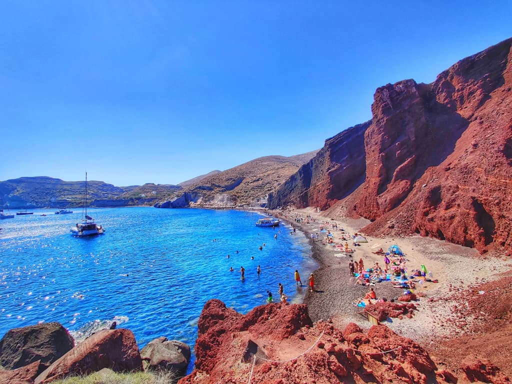 Towering crimson cliffs meeting the dark waters of Red Beach