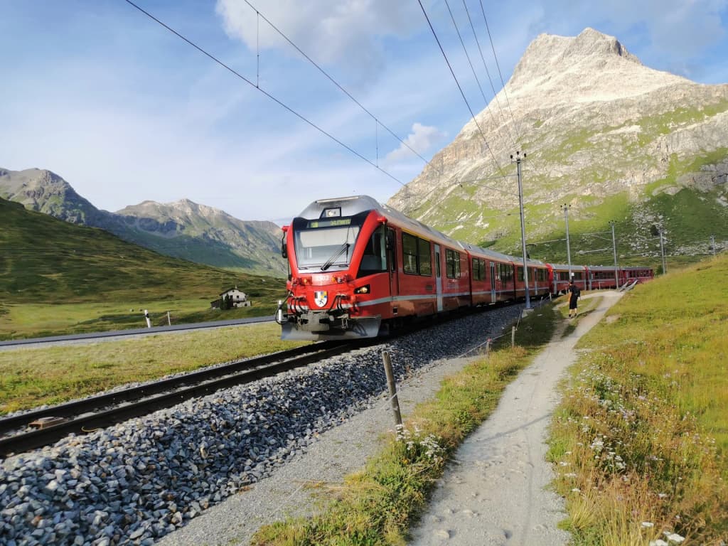 Red regional Bernina train winding through snowy Swiss Alps