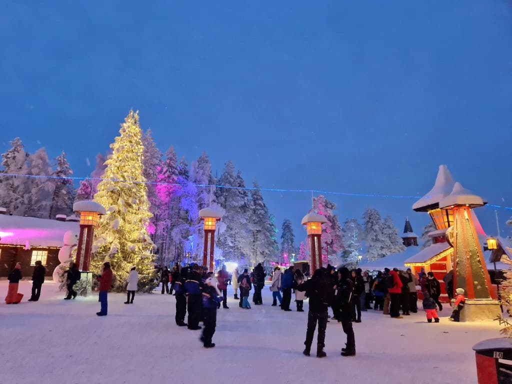 Santa Claus Village main square, families bundled up, Christmas lights everywhere