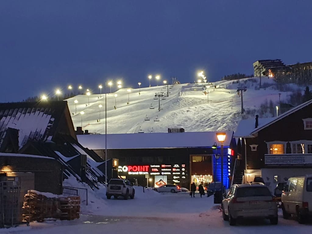 Skiers and snowboarders on the snowy slopes of Levi, with the sun low on the horizon