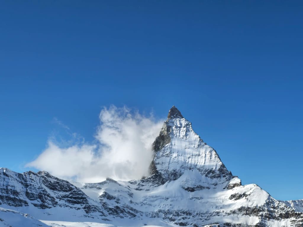 Um pequeno avião sobrevoando os picos recortados do Matterhorn nos Alpes, com nuvens dramáticas e luz do sol