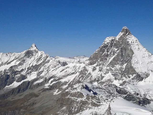 Uma vila de pedra no alto de uma montanha da Córsega, com colinas verdes e céu azul