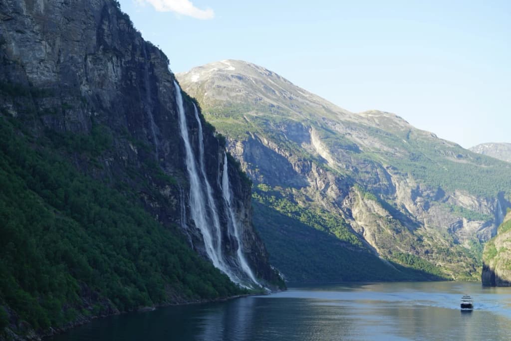Hiker standing on a rocky outcrop above a deep blue fjord